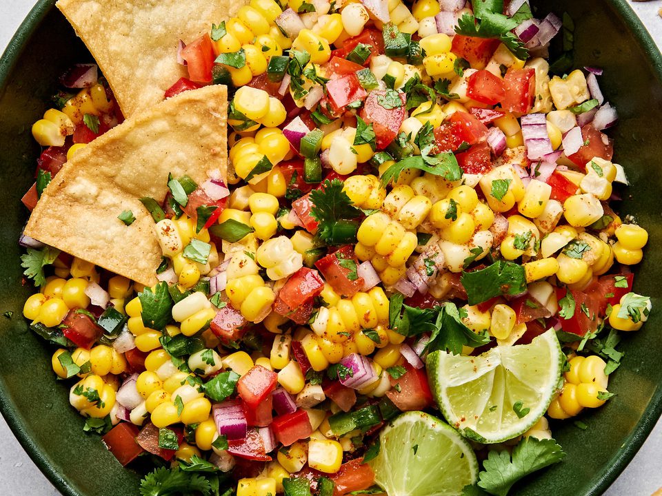 Bowl of fresh corn salsa with diced tomatoes, red onion, jalapeño, cilantro, and lime surrounded by crispy tortilla chips