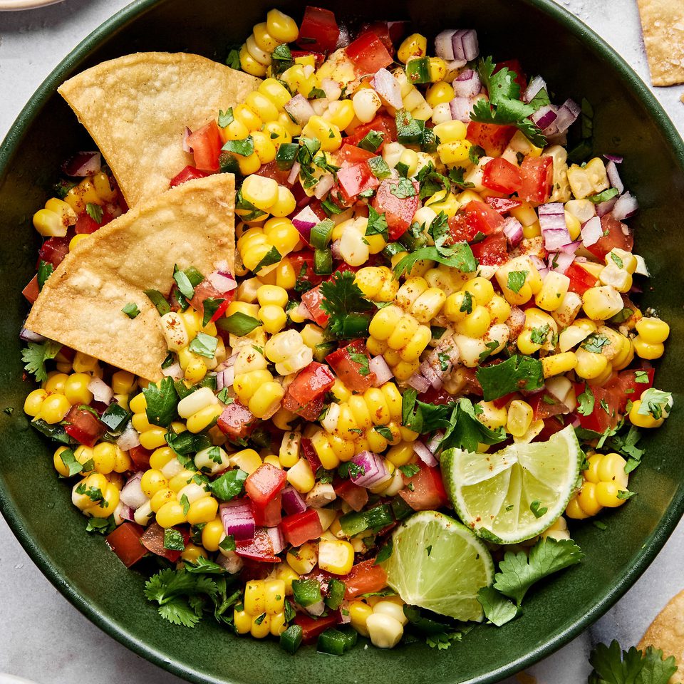 Bowl of fresh corn salsa with diced tomatoes, red onion, jalapeño, cilantro, and lime surrounded by crispy tortilla chips