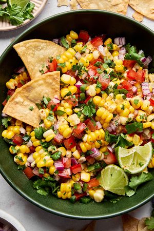 Bowl of fresh corn salsa with diced tomatoes, red onion, jalapeño, cilantro, and lime served with crispy tortilla chips