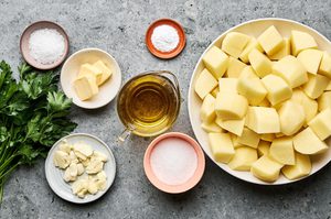 Ingredients for crispy roasted potatoes laid out, including baking soda, potatoes, parsley, olive oil, garlic & salt
