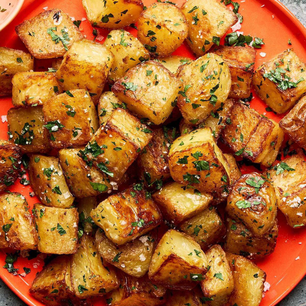 A platter of golden, crispy roasted potatoes garnished with fresh parsley and sprinkled with flaky sea salt.