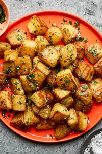 A platter of golden, crispy roasted potatoes garnished with fresh parsley and sprinkled with flaky sea salt.
