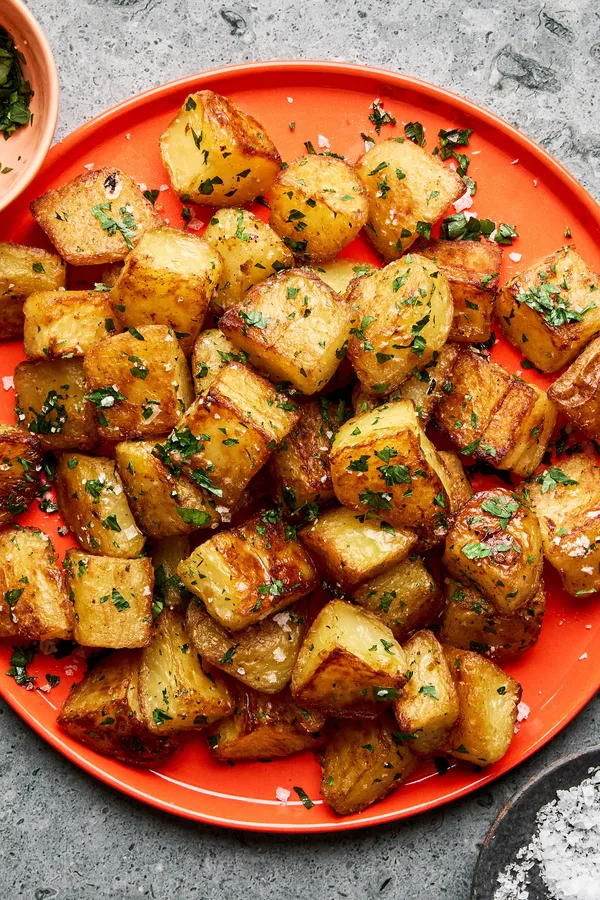 A platter of golden, crispy roasted potatoes garnished with fresh parsley and sprinkled with flaky sea salt.