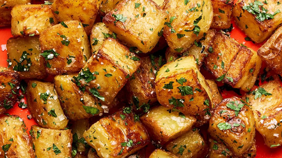 A platter of golden, crispy roasted potatoes garnished with fresh parsley and sprinkled with flaky sea salt.