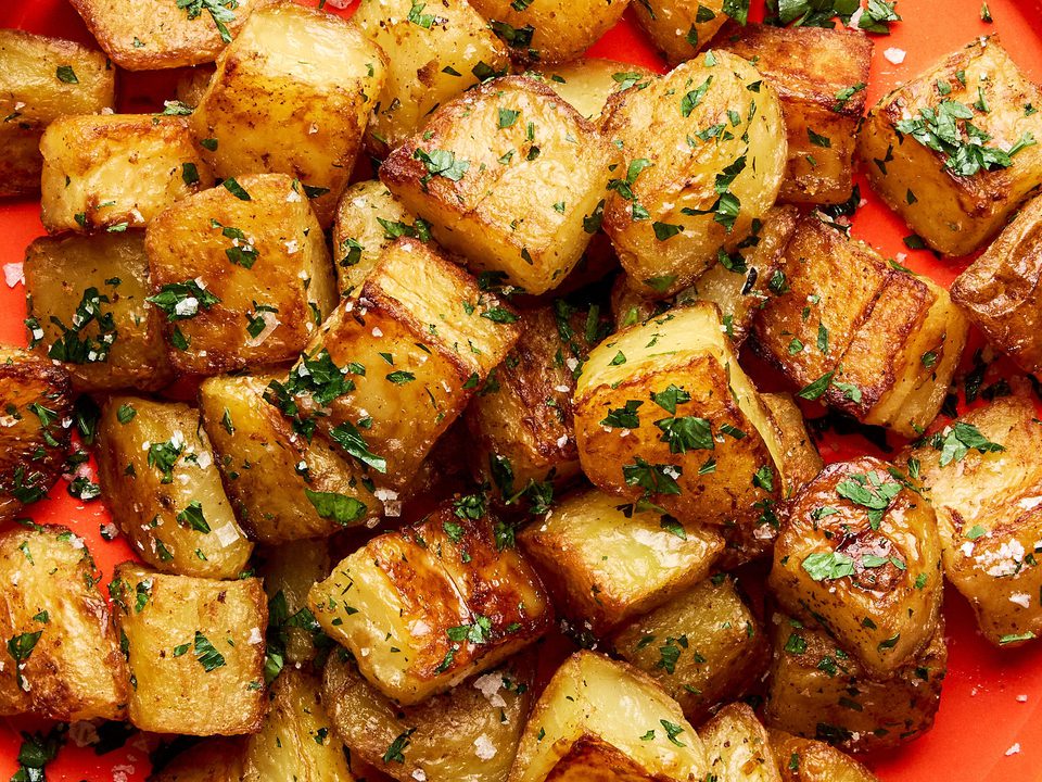 A platter of golden, crispy roasted potatoes garnished with fresh parsley and sprinkled with flaky sea salt.