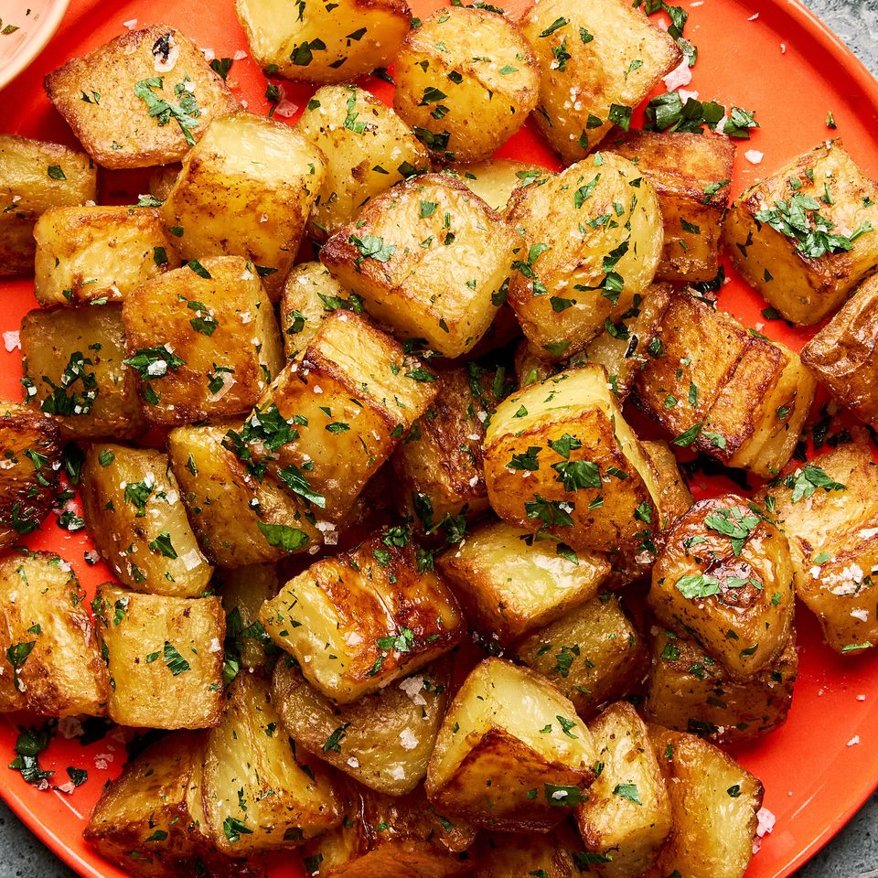 A platter of golden, crispy roasted potatoes garnished with fresh parsley and sprinkled with flaky sea salt.