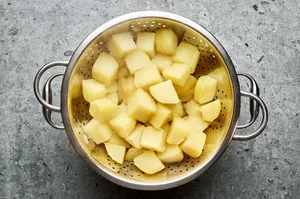 peeled chopped potatoes going into a pot with baking soda and water to make crispy roasted potatoes