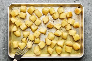 boiled potatoes being tossed in heated olive oil, butter and garlic on a sheet pan