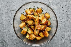 crispy roasted potatoes being tossed in a bowl with fresh parsley and flaky salt before moving to a serving platter