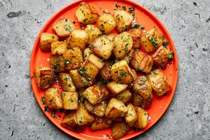 A platter of golden, crispy roasted potatoes garnished with fresh parsley and sprinkled with flaky sea salt.