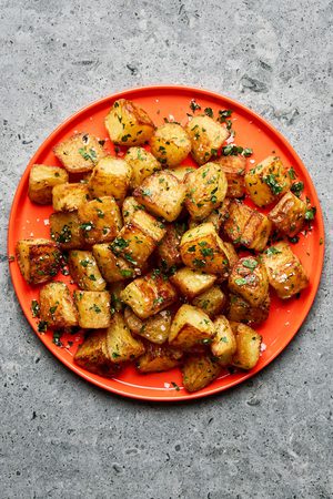 A platter of golden, crispy roasted potatoes garnished with fresh parsley and sprinkled with flaky sea salt.