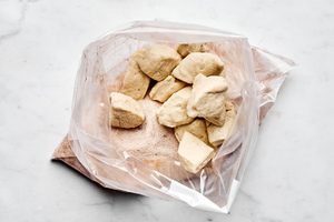 biscuit dough pieces being tossed with sugar and cinnamon until fully coated to make delicious homemade monkey bread