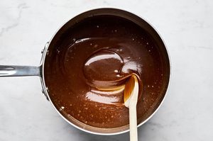 smooth brown sugar butter sauce being stirred in a saucepan ready to be poured into a bundt pan with cinnamon biscuit pieces