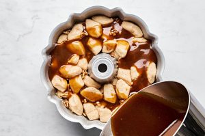 butter and brown sugar sauce being poured over cinnamon sugar coated biscuit pieces in a bundt pan to make monkey bread