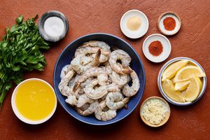 ingredients for garlic butter grilled shrimp laid out in bowl including shrimp, butter, spices and parsley