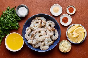 ingredients for garlic butter grilled shrimp laid out in bowl including shrimp, butter, spices and parsley