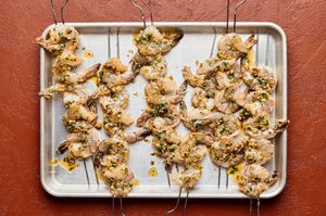 raw shrimp tossed with melted butter and spices being threaded onto skewers to cook on the grill