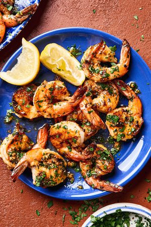 Garlic butter grilled shrimp sprinkled with fresh parsley served on a plate with lemon wedges,a perfect summer seafood meal