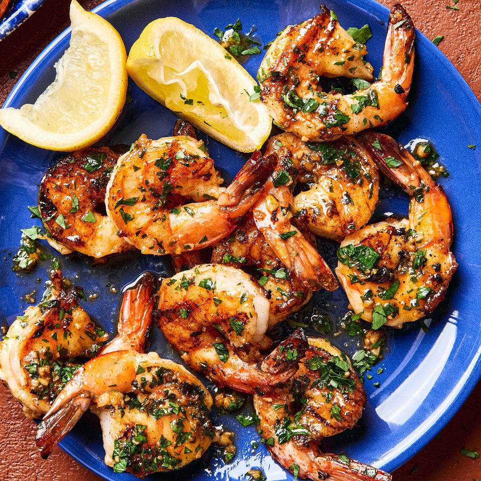 Garlic butter grilled shrimp sprinkled with fresh parsley served on a plate with lemon wedges,a perfect summer seafood meal