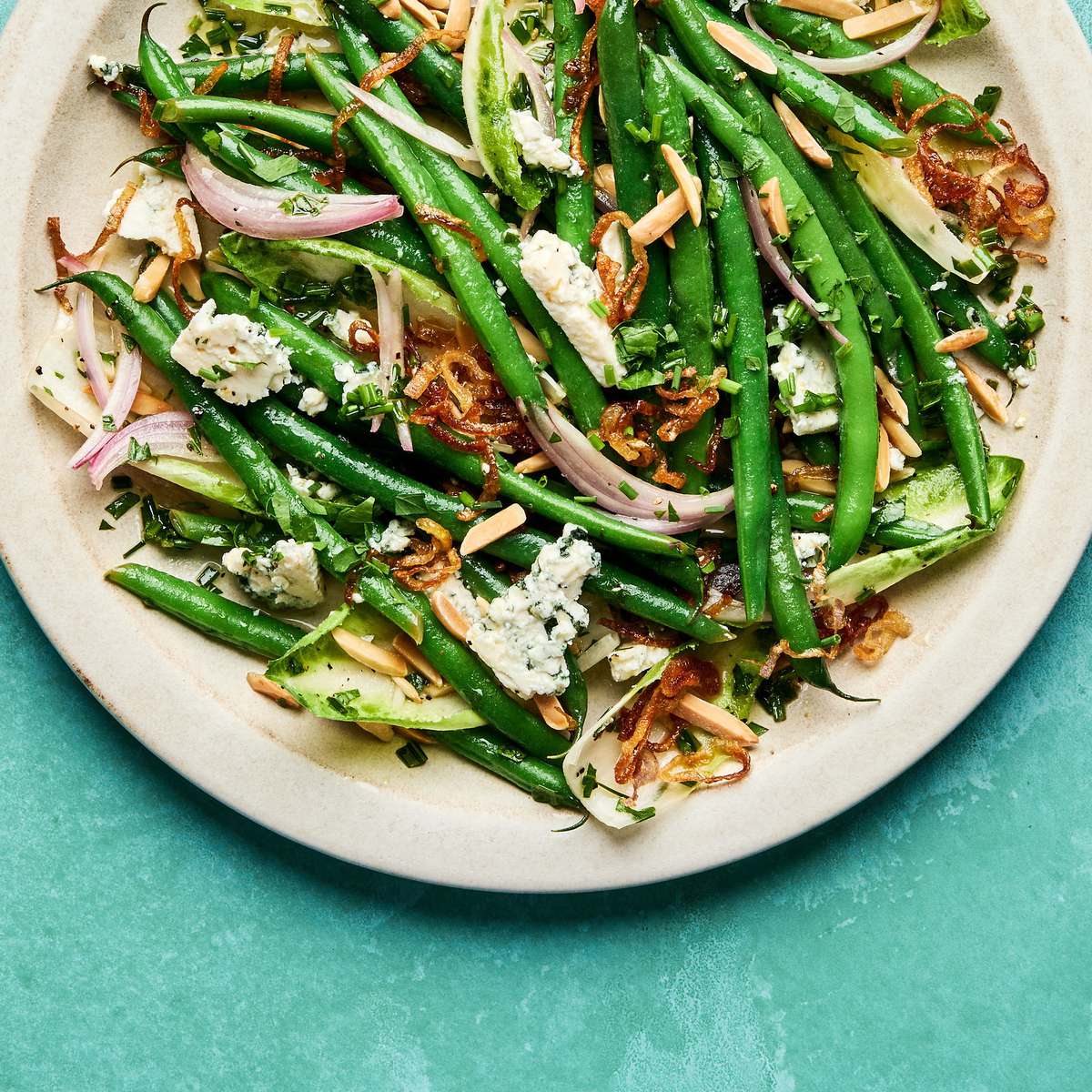 A vibrant green bean salad tossed in a honey Dijon dressing, topped with toasted almonds, blue cheese and fried shallots