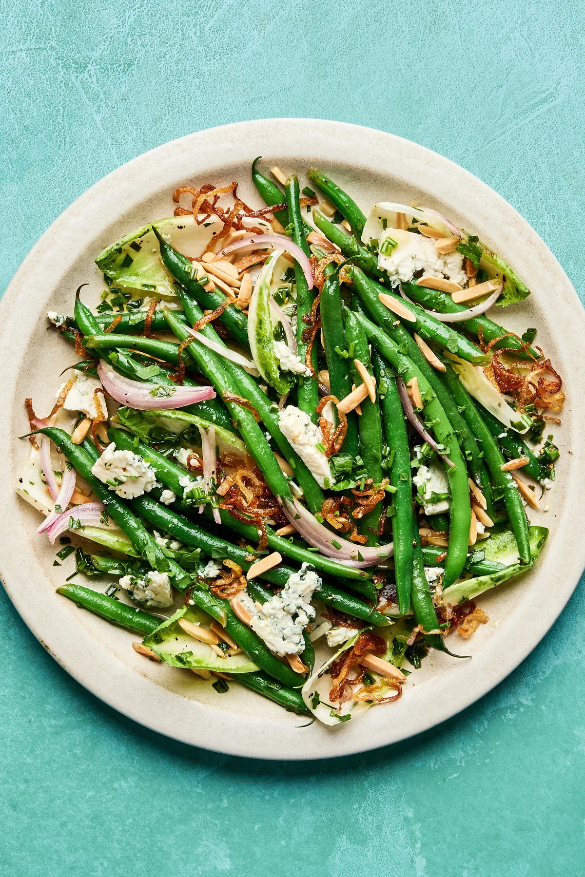 A vibrant green bean salad tossed in a honey Dijon dressing, topped with toasted almonds, blue cheese and fried shallots