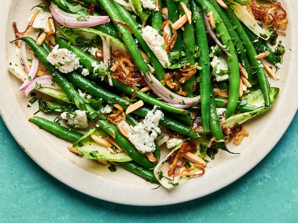 A vibrant green bean salad tossed in a honey Dijon dressing, topped with toasted almonds, blue cheese and fried shallots