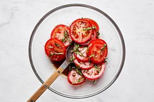 marinated tomatoes being made in a bowl with balsamic, basil, olive oil and garlic