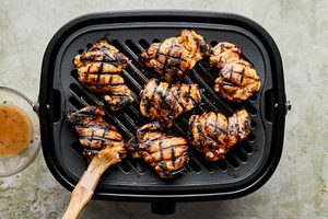marinated chicken thighs being cooked on a grill and brushed with reserved marinade