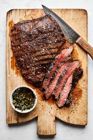 Juicy grilled flank steak sliced on a cutting board, marinated with apple cider vinegar, olive oil and spices