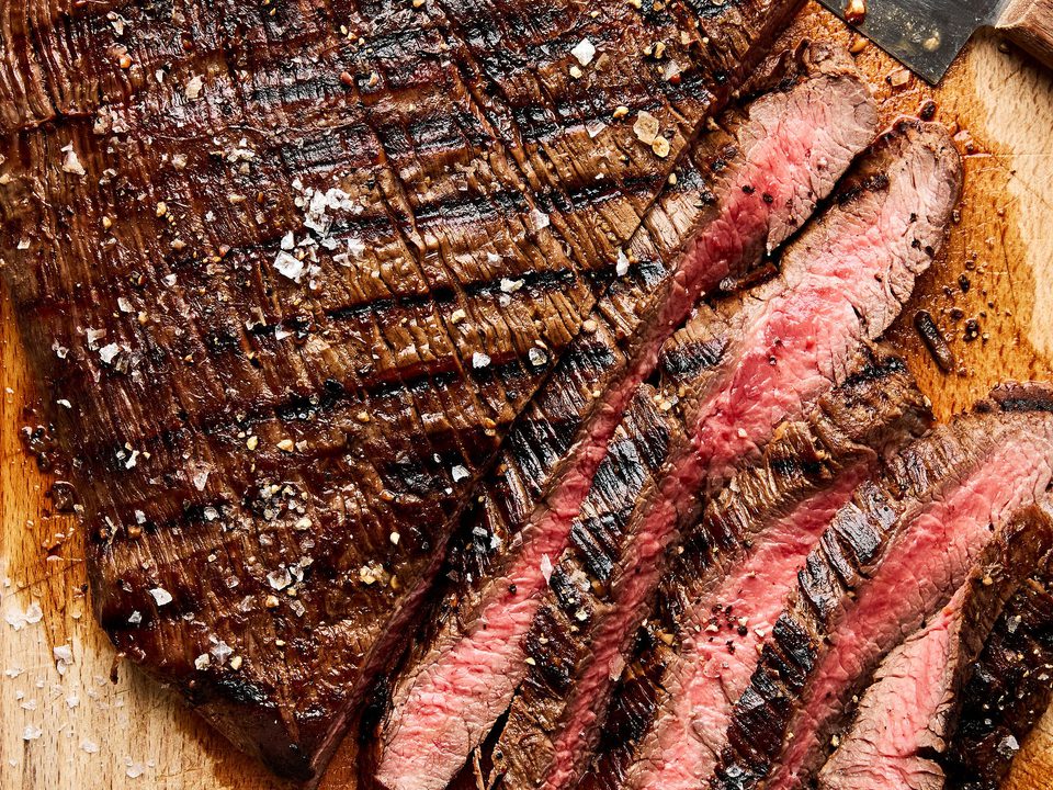 Juicy grilled flank steak sliced on a cutting board, marinated with apple cider vinegar,  olive oil and spices