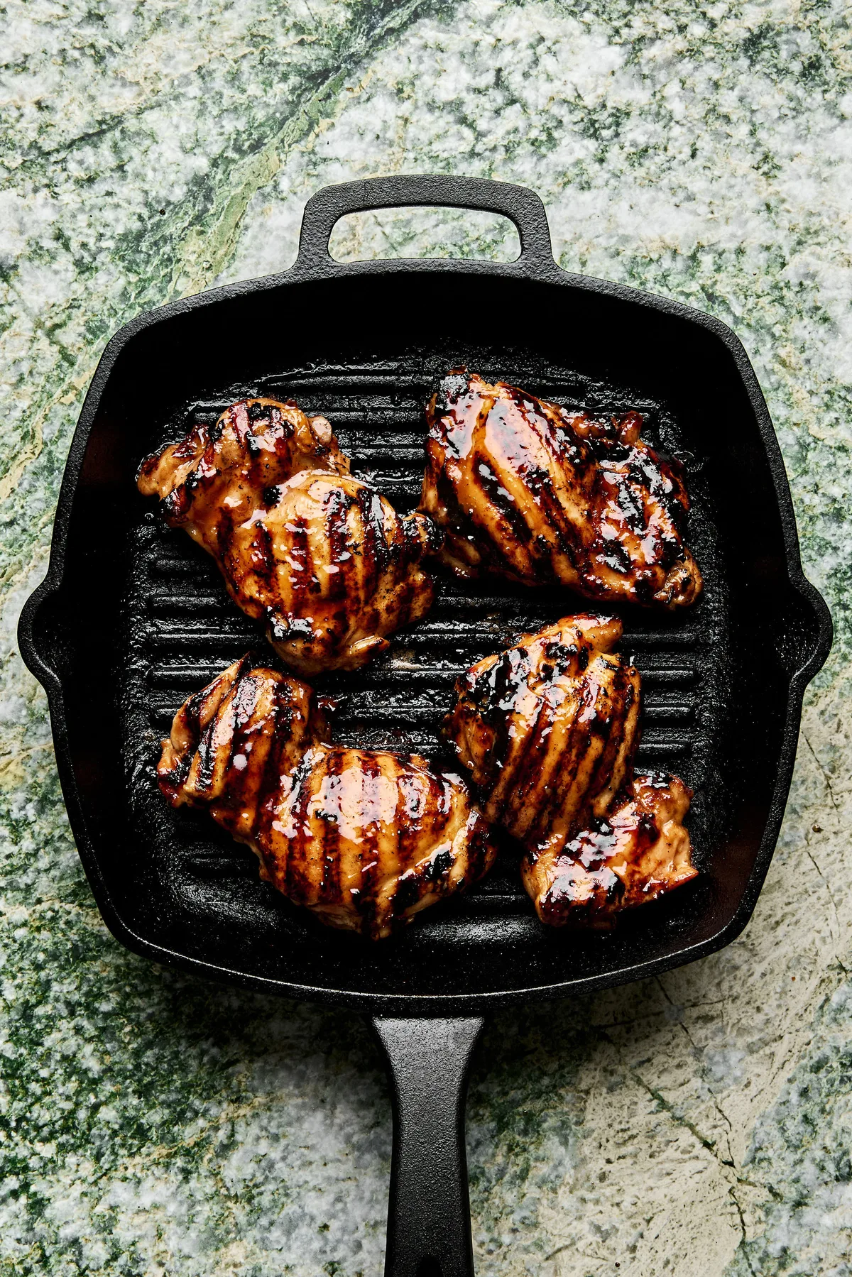 rilled teriyaki chicken cooking on a hot grill, with char marks and glaze caramelizing on the surface