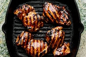 rilled teriyaki chicken cooking on a hot grill, with char marks and glaze caramelizing on the surface