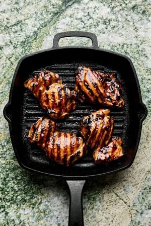 rilled teriyaki chicken cooking on a hot grill, with char marks and glaze caramelizing on the surface