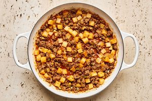a simple one pot dinner of ground beef and potatoes in a skillet ready to be topped with cheddar cheese