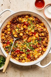 A hearty one-pot dish of ground beef and diced potatoes, topped with melted cheddar cheese and sliced green onions.