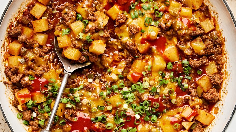 A hearty one-pot dish of ground beef and diced potatoes, topped with melted cheddar cheese and sliced green onions.
