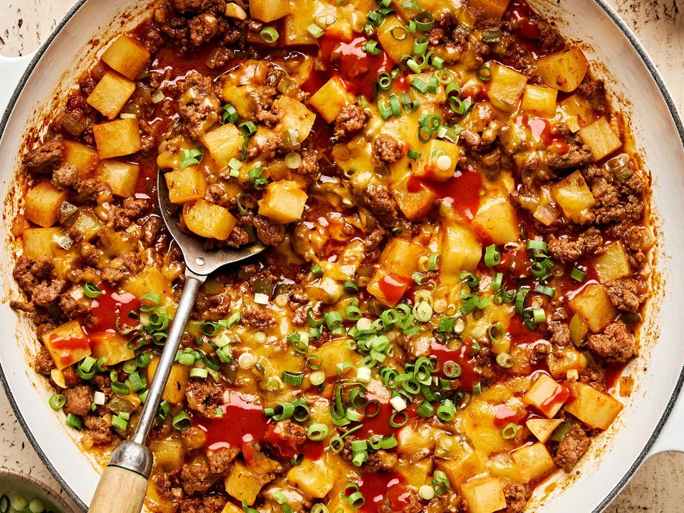 A hearty one-pot dish of ground beef and diced potatoes, topped with melted cheddar cheese and sliced green onions.