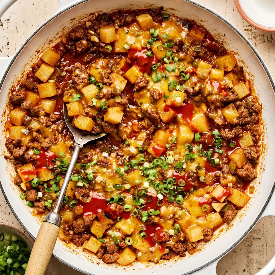 A hearty one-pot dish of ground beef and diced potatoes, topped with melted cheddar cheese and sliced green onions.
