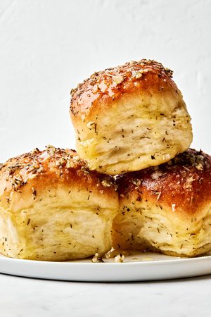 3 Freshly baked Rhodes rolls brushed with golden herby butter stacked on a plate