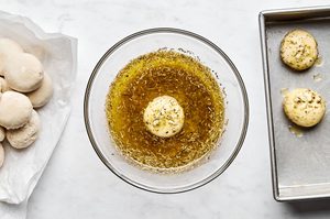 raw rhodes rolls being rolled in homemade garlic and herb butter