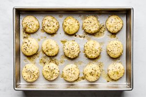raw rhodes rolls covered with garlic and herb butter on a pan to thaw and rise before baking
