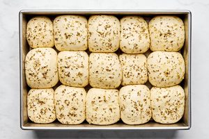 raw rhodes rolls covered with garlic and herb butter on a pan rising before baking