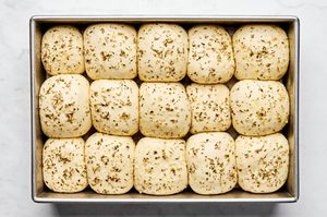 raw rhodes rolls covered with garlic and herb butter on a pan rising before baking
