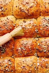 freshly baked dressed up rhodes rolls being brushed with melted herby butter and sprinkled with flaky salt