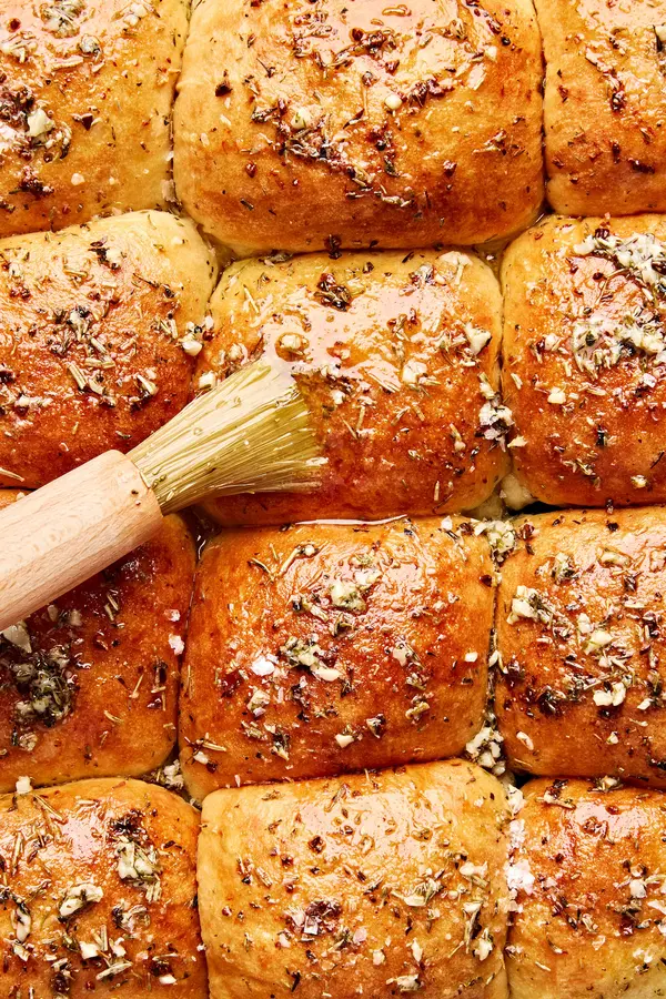freshly baked dressed up rhodes rolls being brushed with melted herby butter and sprinkled with flaky salt