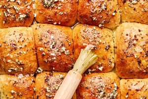 freshly baked dressed up rhodes rolls being brushed with melted herby butter and sprinkled with flaky salt