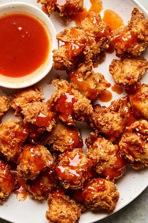 Crispy hot honey chicken nuggets drizzled with spicy sweet glaze on a plate, served with extra hot honey sauce for dipping