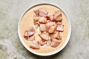 raw chicken breast pieces being dredged in an egg and buttermilk mixture