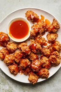 Crispy hot honey chicken nuggets drizzled with spicy sweet glaze on a plate, served with extra hot honey sauce for dipping