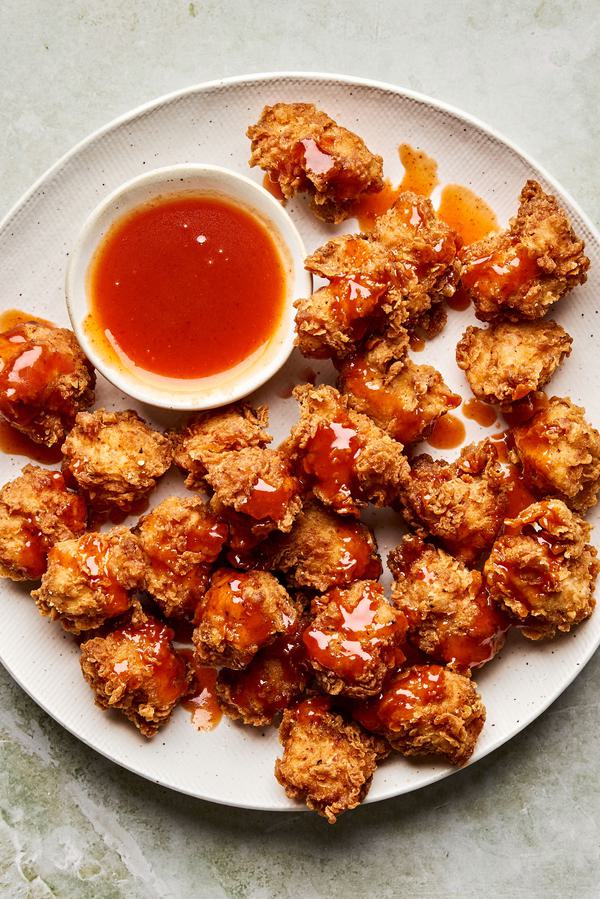 Crispy hot honey chicken nuggets drizzled with spicy sweet glaze on a plate, served with extra hot honey sauce for dipping
